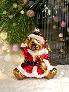 Teddy bear figurine dressed as Santa sitting on white fabric under pine branches