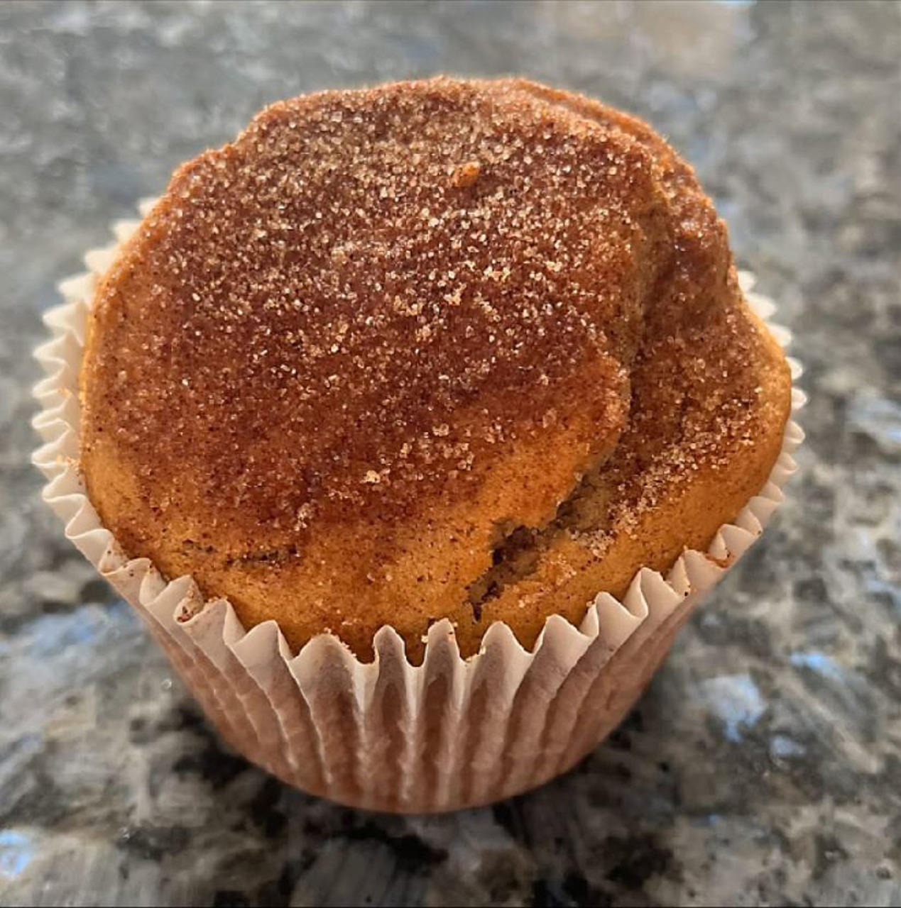 Close-up of a cinnamon sugar coated muffin in a paper liner on granite countertop