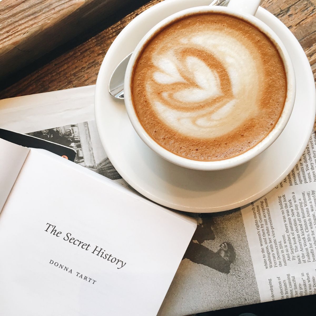 Latte with heart foam art beside an open book on a wooden table