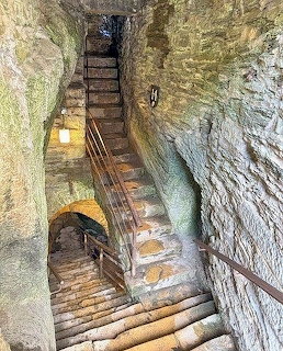 Steep stone stairs inside a narrow medieval castle passage with rough rock walls