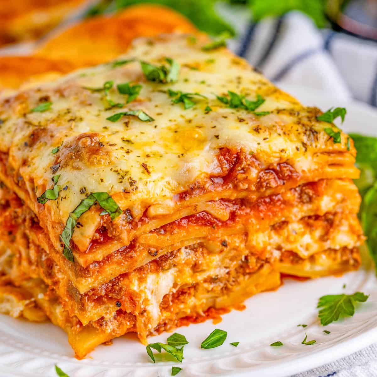 Slice of baked lasagna with melted cheese, meat sauce layers, and fresh herb garnish on white plate