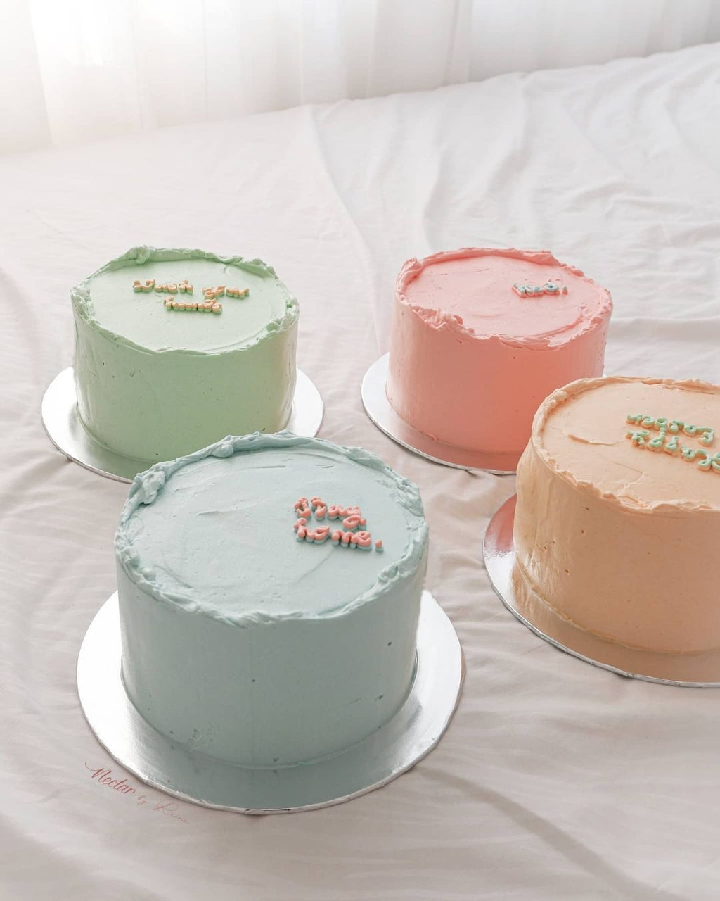 Four round cakes with pastel colored frosting on white fabric background