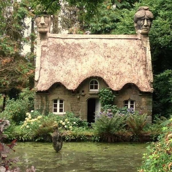 Stone cottage with thatched roof and two statue figures in garden setting