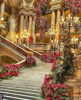Grand staircase of an ornate opera house decorated with red flowers, golden columns and chandeliers