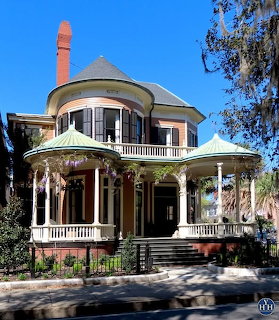 Victorian house with round turret, green copper rofs, wraparound porch, and brick chimney under blue sky