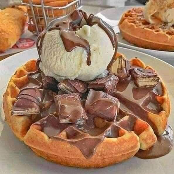 Waffle topped with vanilla ice cream and chocolate sauce on a white plate