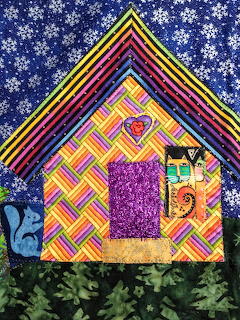 Decorative fabric quilt showing a house made from colorful patchwork patterns on blue starry background