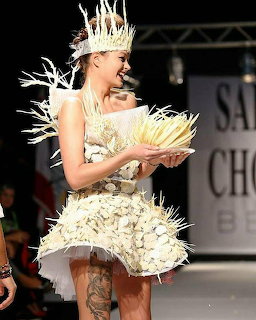 Model on runway wearing a creative white chocolate dress and crown, holding a plate