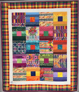 Colorful patchwork quilt with varied fabric patterns in squares bordered by plaid frame