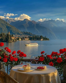 Terrace overlooking lake with red flowers, set table, mountains and boat in background