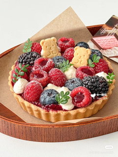 Fruit tart with raspberries, blackberries, blueberries, cream, and bear-shaped cookies on a brown plate