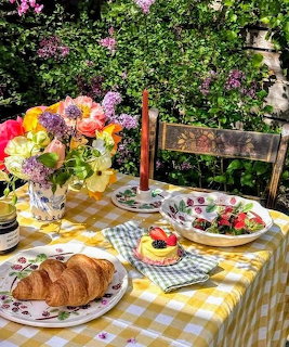 Outdoor brunch table with flowers, croissants, fruit tart, and salad in a sunny garden