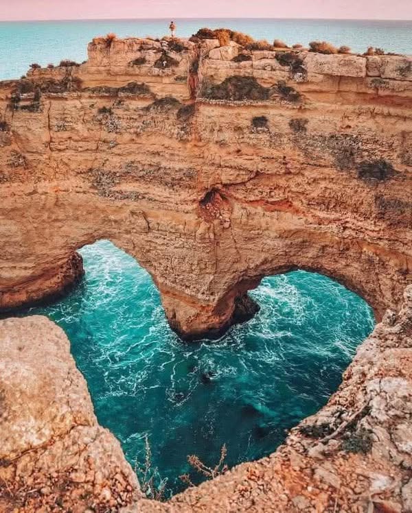 Heart-shaped turquoise water pool carved into red layered rock cliff by the ocean