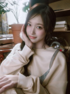 Young Asian woman with dark hair wearing a beige sweatshirt posing indoors near a bookshelf