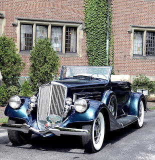 Dark blue 1935 Pierce-Arrow convertible with chrome grille and white wall tires in front of ivy-covered brick building