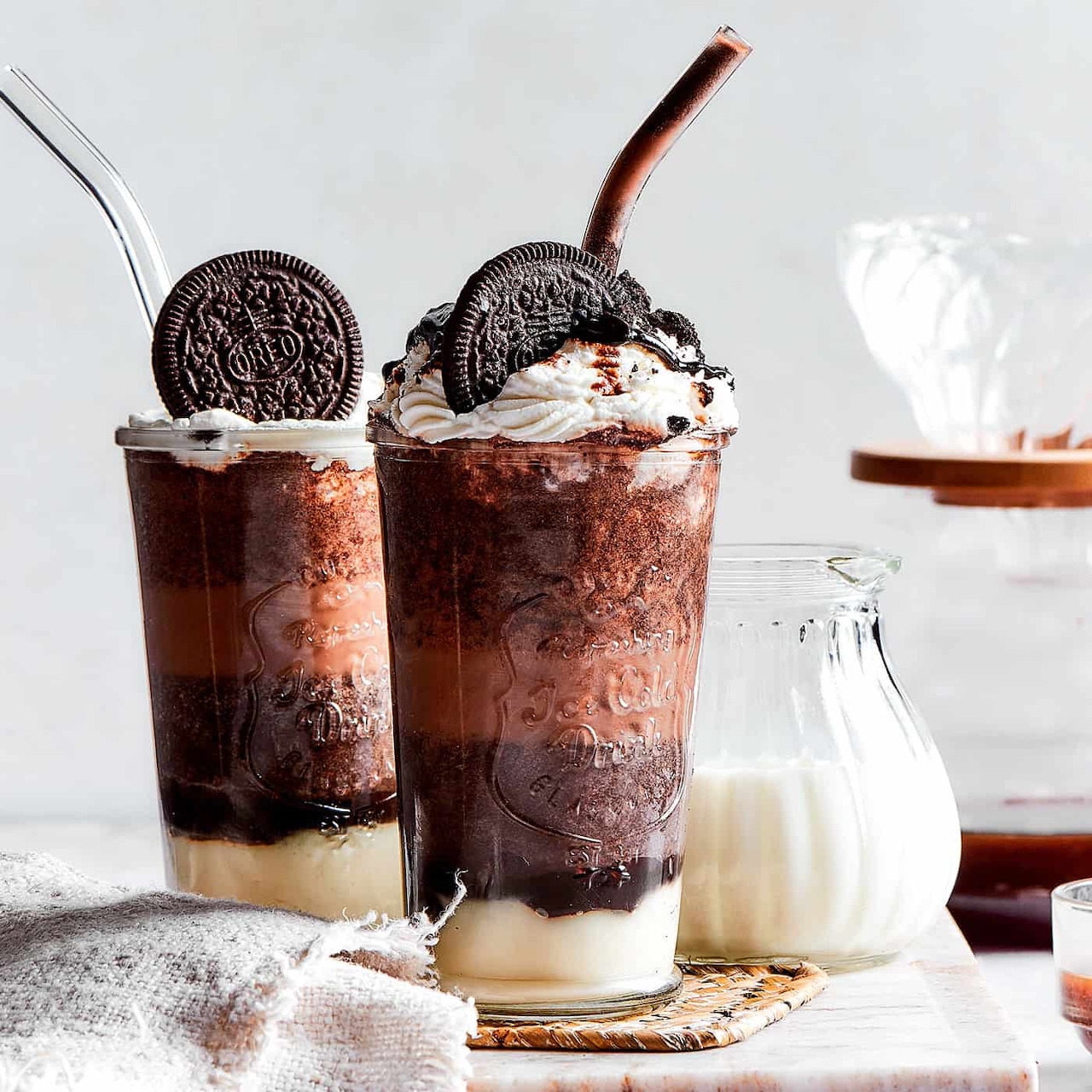 Two layered chocolate drinks with whipped cream and cookies beside a small bottle of milk