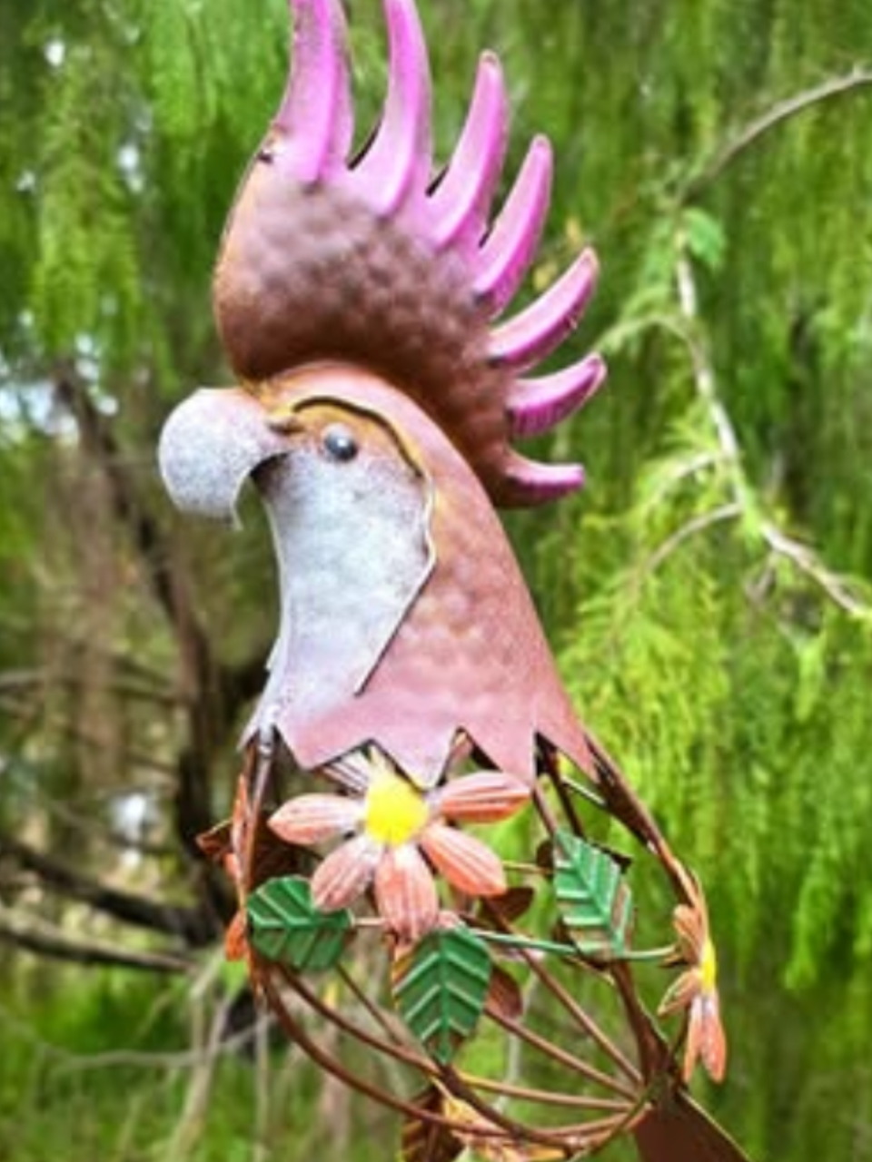 Colorful metal rooster garden sculpture with flower details in front of green foliage