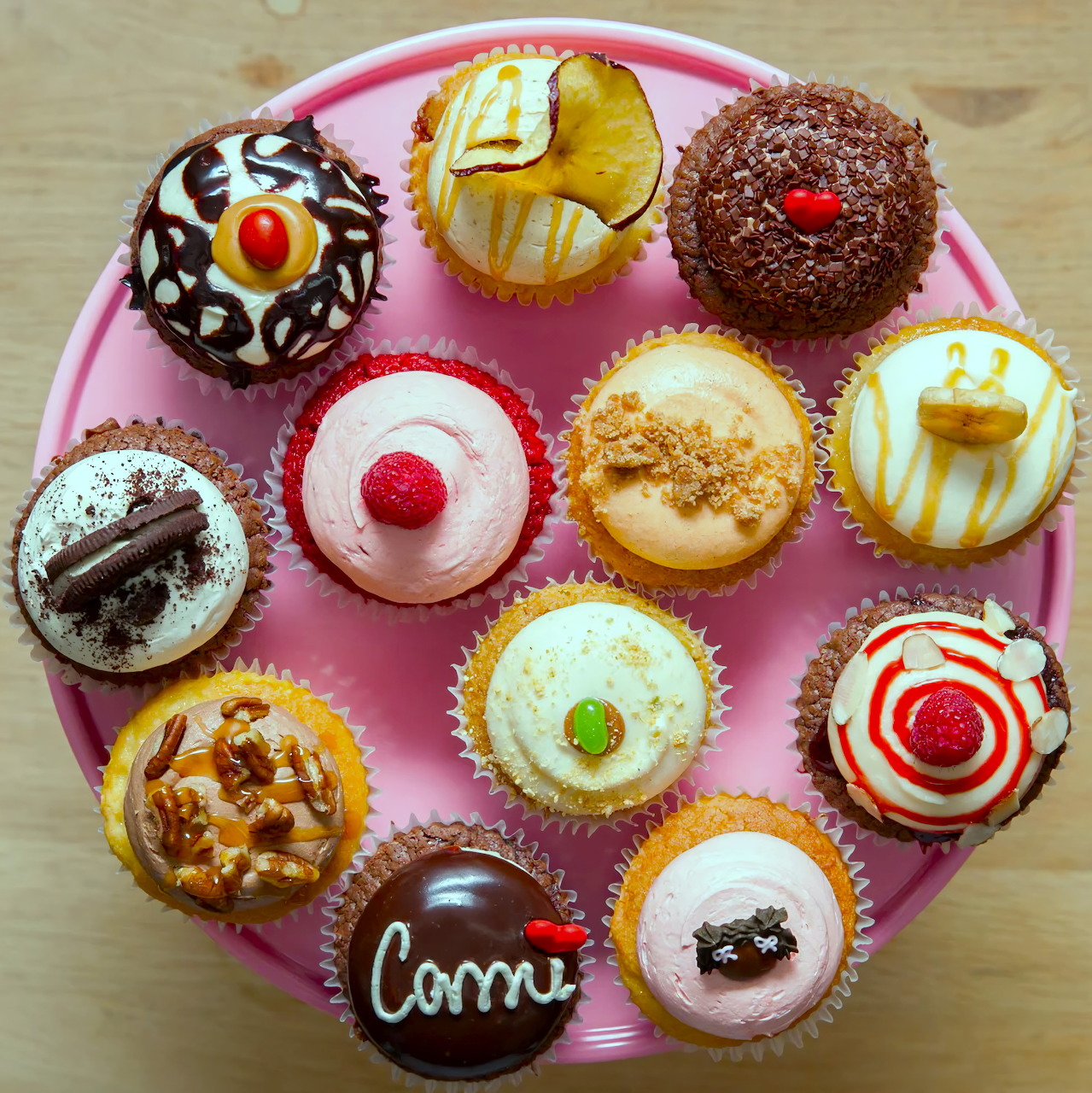 Assorted decorated cupcakes on a pink plate, viewed from above