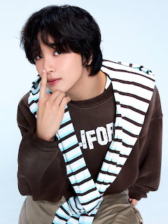 Young man with dark hair posing with finger on lips wearing brown and blue striped layers