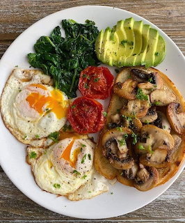 Breakfast plate with sunny-side eggs, mushrooms, avocado, kale, and tomato on white plate