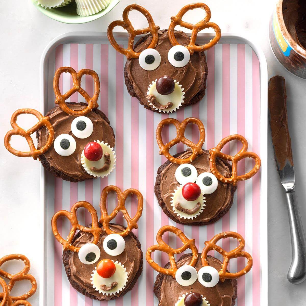 Chocolate reindeer cupcakes with pretzel antlers and candy decorations arranged on a pink striped plate