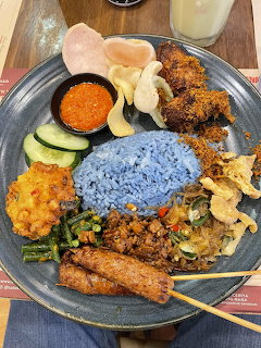 Blue rice meal with fried chicken, vegetables, and condiments on a dark plate