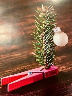 Small pine branch in a red clothespin with a glass bauble on dark wood