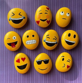 Ten yellow rocks painted with emoji faces on purple striped fabric
