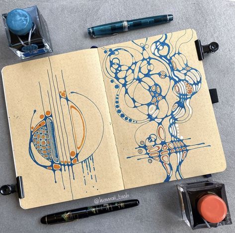 Open sketchbook with blue and orange abstract ink art, fountain pens and ink bottles around it