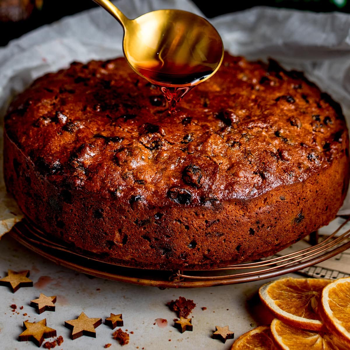 Round fruit cake with syrup drizzle, dried orange slices, and star-shaped cookies