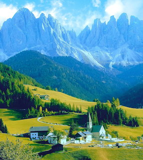 Small alpine village with church in green valley surrounded by dramatic jagged mountain peaks