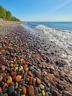 Colorful pebble beach with gentle waves along a lakeshore under a clear blue sky