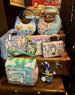 Collection of colorful illustrated handbags arranged on vintage brown suitcases in a shop display