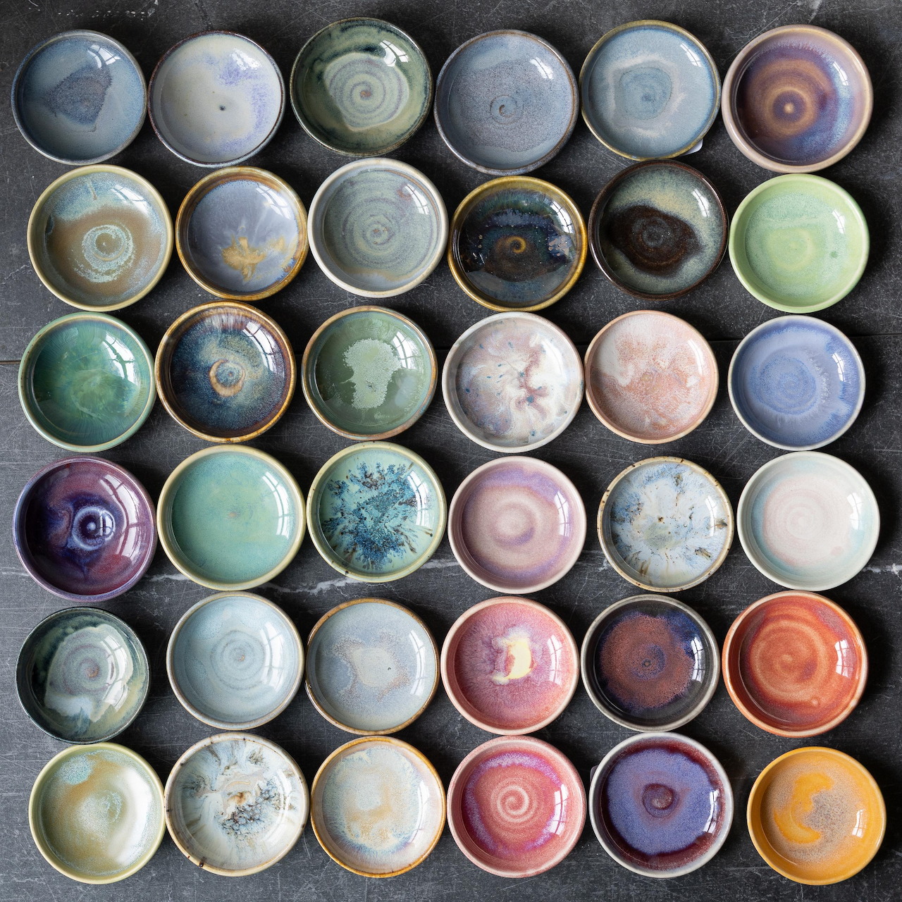 Grid of 42 handmade ceramic bowls with colorful glazes and artisan patterns viewed from above