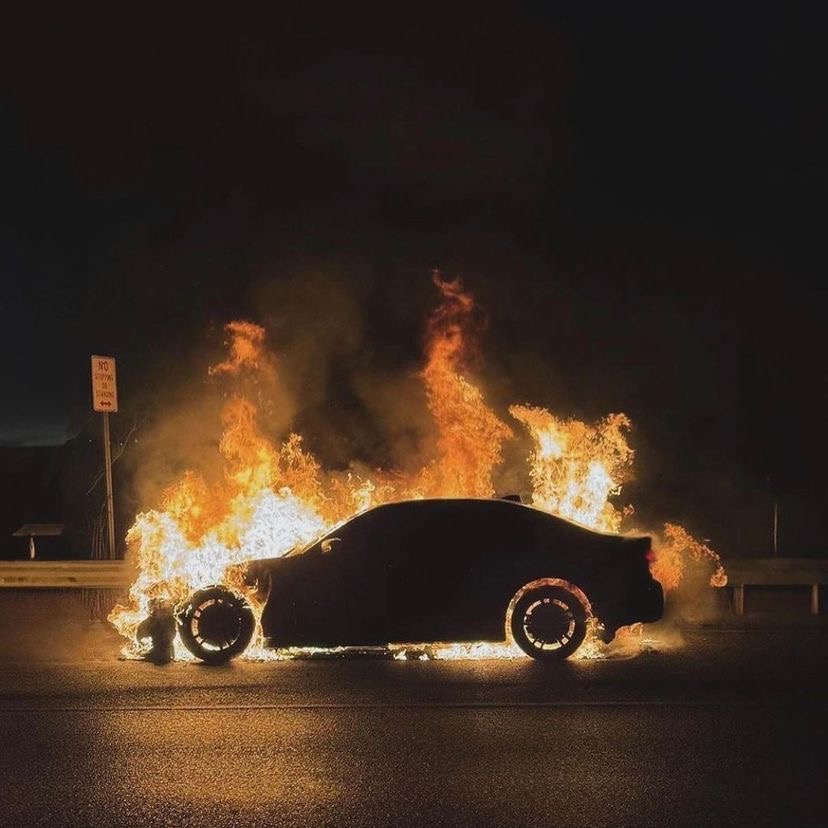 Silhouette of a car on fire at night with flames surrounding it on a road