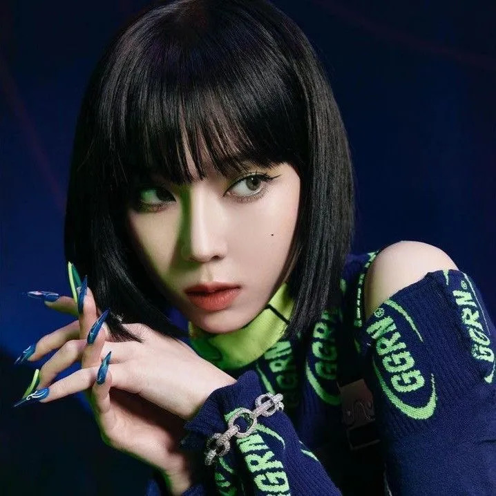 Studio portrait of a woman with a black bob haircut, blue nails, and an off-shoulder dark top