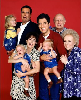 Everybody Loves Raymond TV show cast posing together with babies against a red background