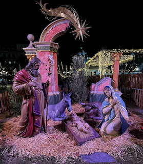 Nativity scene with figures of Mary, Joseph, and baby Jesus illuminated by colorful lights at night