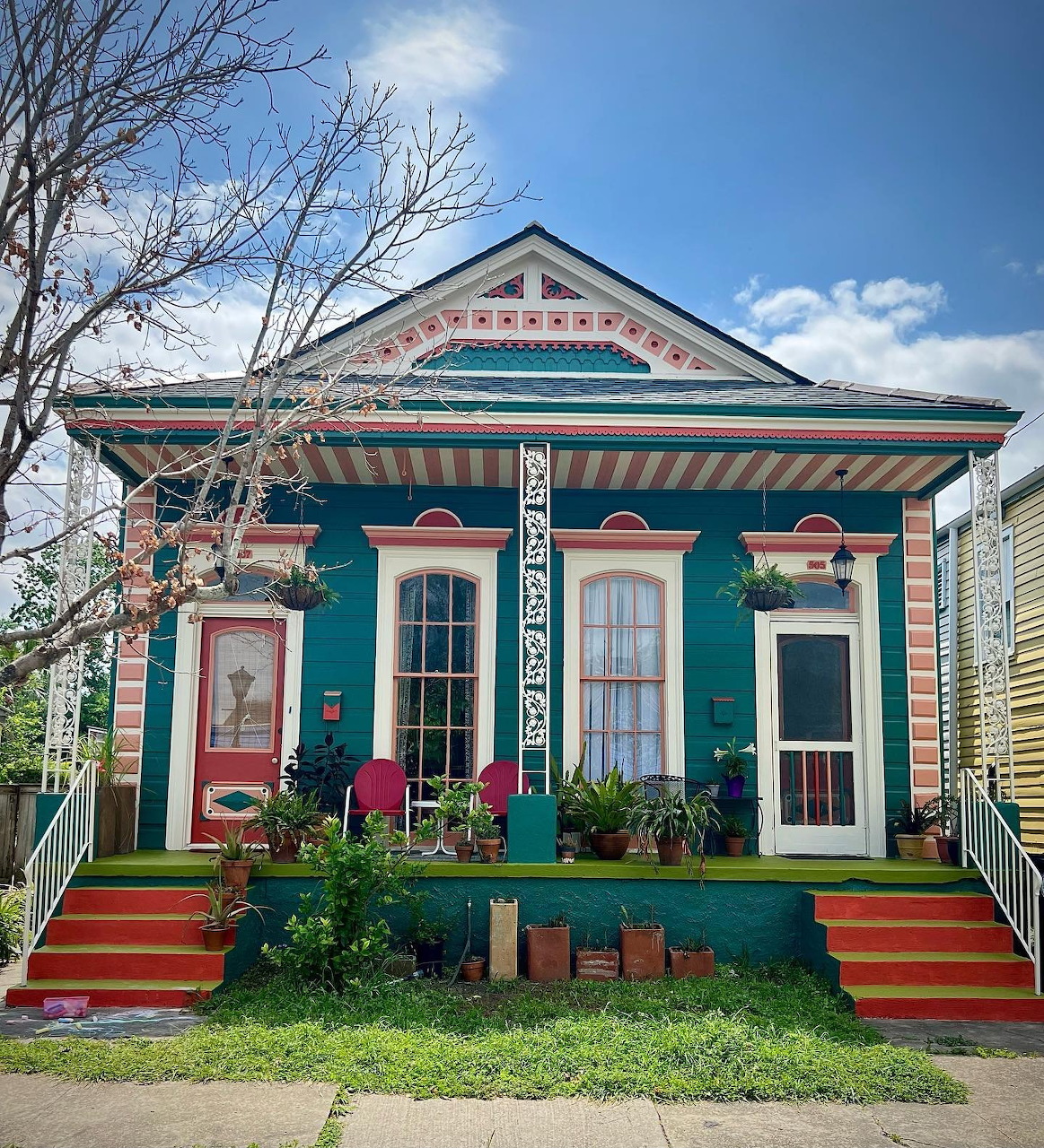 Turquoise Victorian cottage with pink trim, decorative gables, white doors, and red entry stairs