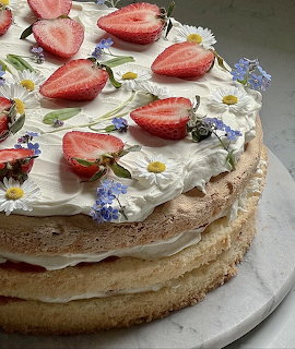 Layered cake with whipped cream, strawberries, and edible flowers on top