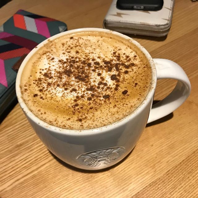 White mug of pumpkin spice latte with cinnamon foam on wooden table