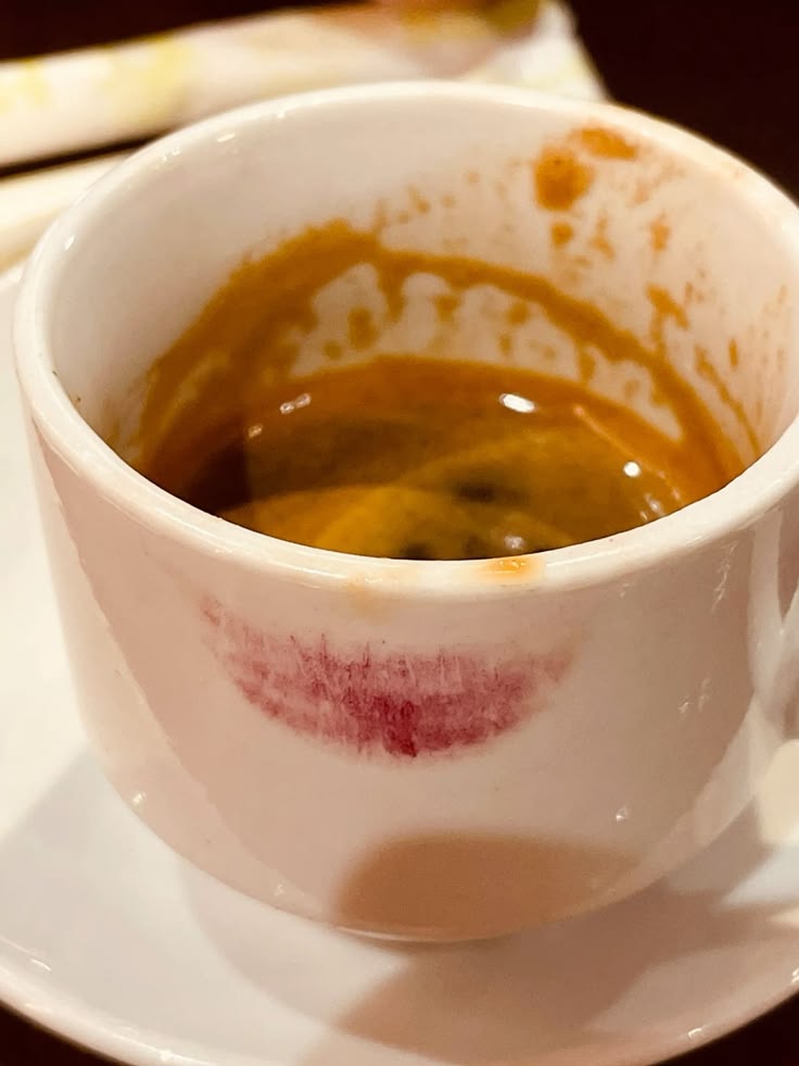 White espresso cup with coffee residue and a lipstick stain on a saucer