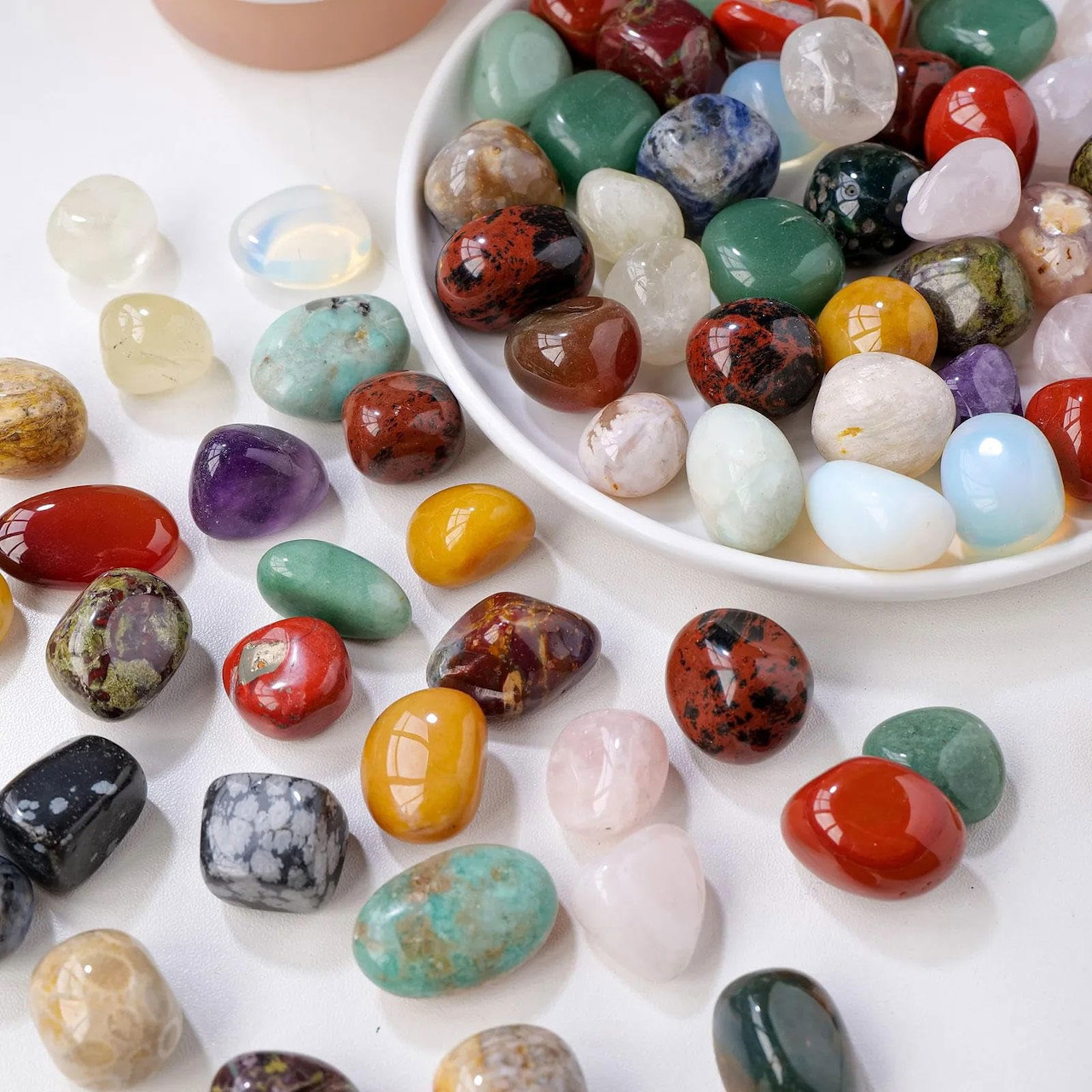 Assorted polished gemstones in multiple colors scattered on white background
