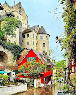 Meersburg Castle on a hill above colorful traditional German buildings with a red-rofed house in foreground