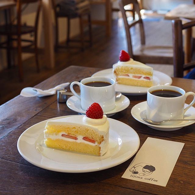 Two plates of strawberry shortcake with coffee cups on a wooden café table