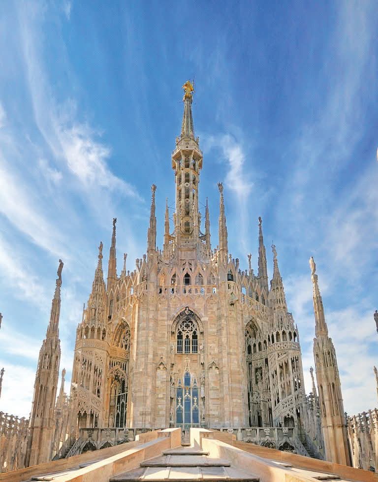Ornate Gothic spires of Milan Cathedral rooftop with golden statue under blue sky
