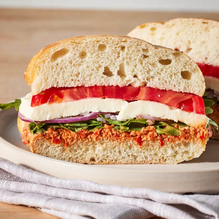 Ciabatta sandwich with mozzarella, tomato, red onion, arugula, and spread on a plate