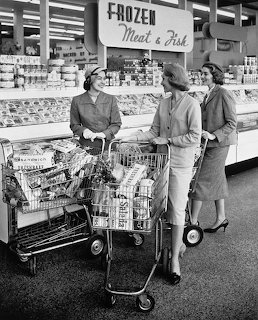 Three women with shopping carts chatting in a vintage grocery store frozen section