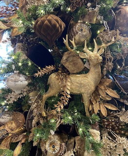 Woodland-themed Christmas tree with a gold deer ornament, pinecones, feathers, and warm lights