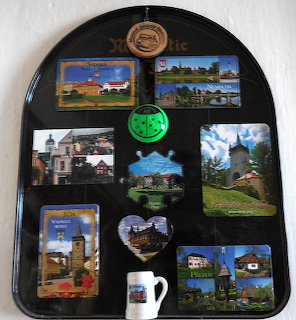 Dark magnetic board with multiple souvenir fridge magnets showing towns, churches, and landscapes